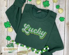 Stay cozy and stylish this St. Patrick's Day with our forest green lucky retro sweatshirt.  Featuring a beautiful watercolor vintage design, this Irish sweater is perfect way to show off your heritage and get into the holiday sprirt.  The simple design and lucky word vintage graphic make it easy to pair with any outfit, while the comfortable crewneck cut and soft fabric ensure that your stay comfortable all day long.   This lucky word hoodie is the perfect way to embrace Irish heritage.    For m Green Hoodie With Letter Embroidery For Fall, Green Crew Neck Hoodie With Embroidered Graphics, Green Embroidered Fall Hoodie, Green Letter Embroidery Sweatshirt For Fall, Green Sweatshirt With Letter Embroidery For Fall, Irish Embroidery, Custom Embroidered Sweatshirt, Irish Sweater, Custom Sweaters