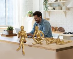 a man sitting at a kitchen counter working on his laptop next to gold figurines