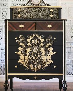 an ornate black and gold chest of drawers with decorative designs on the front, along with two white pillows