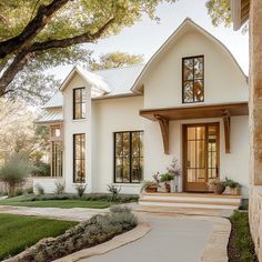 a white house with lots of windows and plants on the front porch, surrounded by green grass