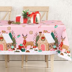 a pink table cloth with reindeers and houses on it, sitting in front of two wooden chairs