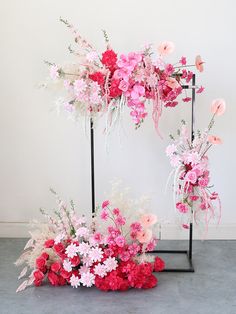 an arrangement of pink and white flowers on a black metal stand in front of a white wall