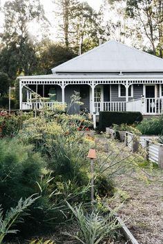 an old house is surrounded by flowers and plants in the foreground, with a white picket fence around it