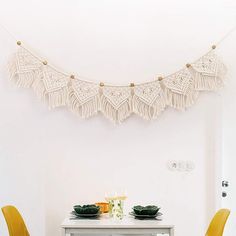 a white table with two yellow chairs and a string of tassels hanging from the ceiling