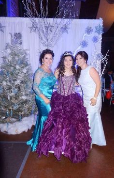 three women in dresses standing next to each other near a christmas tree and decorated wall