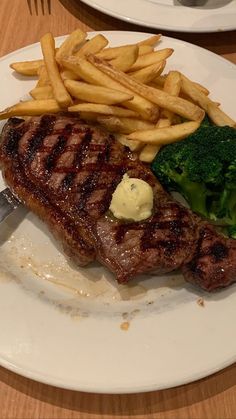 steak, fries and broccoli on a white plate at a table with utensils