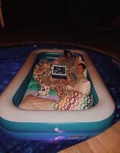 two people laying in an inflatable pool with a laptop