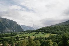 a lush green valley surrounded by mountains and trees on a cloudy day with white clouds in the sky