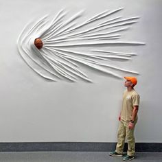 a man standing in front of a white wall with a basketball on top of it