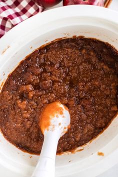 a white bowl filled with chili and topped with an orange sauce next to some apples