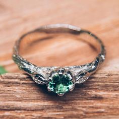 a close up of a ring with a green stone in it on a wooden surface