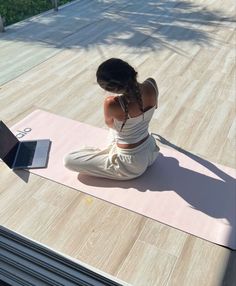 a woman sitting on top of a yoga mat using a laptop computer