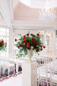 a vase filled with red flowers sitting on top of a white table covered in chairs