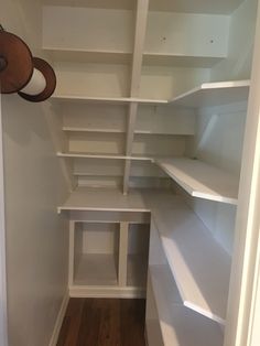 an empty walk in closet with white shelving and wood flooring on the side