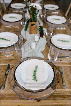 the table is set with white plates and silverware, green napkins and greenery