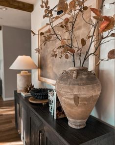 a vase sitting on top of a wooden table in front of a wall with a painting