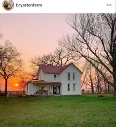 a white house sitting in the middle of a field with trees and grass around it