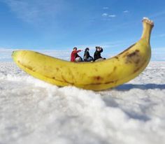 three people are sitting on top of a banana in the middle of some white snow