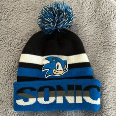 a blue and black sonic hat with the word sonic on it, sitting on a gray blanket