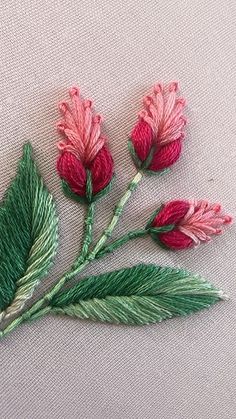 three pink flowers with green leaves on a white cloth covered surface, one is embroidered onto the fabric and the other has been stitched together