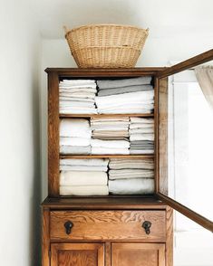 a wooden cabinet filled with lots of folded white towels and a wicker basket on top of it