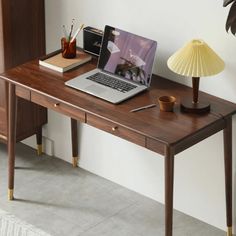 a laptop computer sitting on top of a wooden desk next to a lamp and other items