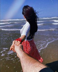 a man holding the hand of a woman on top of a sandy beach next to the ocean