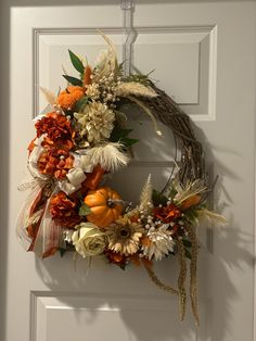 a wreath is hanging on the front door with flowers and leaves around it, as well as pumpkins