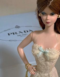 a close up of a doll wearing a dress and holding a handbag in front of a sign