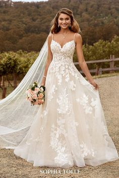 a woman in a wedding dress with a veil over her head standing on a dirt road