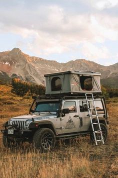 a jeep with a tent on top parked in a field next to mountains and trees