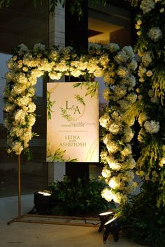 a sign that is surrounded by flowers and greenery in front of a building at night