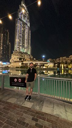 a man standing on the edge of a bridge next to a body of water at night