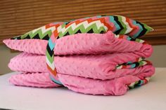 stack of pink and green cloths on top of a white table with wooden blinds in the background