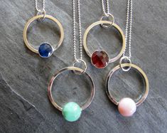 Here are four necklaces made with sterling silver and gemstones. The circles are made of square wire that I formed into a circle and soldered closed.  I added a ring that serves as a bail and a gemstone set in a silver cup setting.  The dainty sterling silver bead chain is included. The circles measure approx. 1" in diameter. The gemstones are 10 mm pink opal, 10mm  faceted chrysoprase, 10mm faceted garnet, and 8mm faceted iolite. The chains are 18" long with lobster clasps. Modern Round Jewelry With Unique Variations, Modern Wire Wrapped Round Jewelry, Modern Round Wire Wrapped Jewelry, Faceted Sterling Silver Square Pendant Jewelry, Sterling Silver Faceted Square Pendant Jewelry, Silver Circle Gemstone Jewelry, Sterling Silver Circle Birthstone Jewelry, Silver Circle Jewelry With Birthstone, Modern Sterling Silver Jewelry With Round Stone