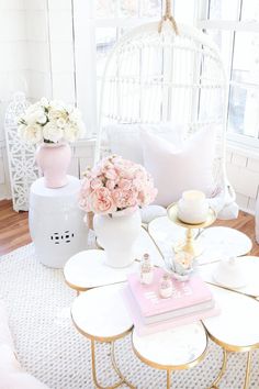 a living room with white furniture and flowers in vases on the coffee table next to a window