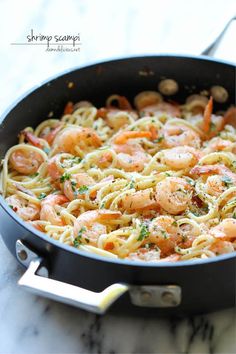 a pan filled with pasta and shrimp on top of a table next to a phone