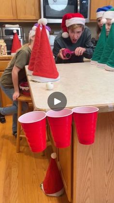 kids in santa hats sitting at a kitchen table with red cups on it and one boy looking at the camera