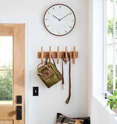 a clock mounted to the side of a wall next to a purse and coat rack