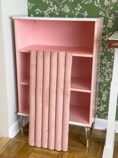 a pink bookcase with six books on it in front of a floral wallpaper