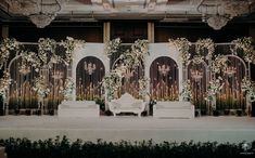 a stage set up for a wedding with white flowers and greenery on the wall