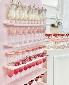 there are many wine glasses on the shelves with flowers in them and one is filled with pink liquid