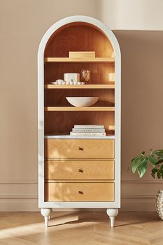 a wooden cabinet with two drawers and a bowl on the top, next to a potted plant