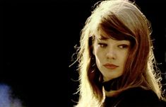 a woman with long hair and bangs standing in front of a black background, looking at the camera