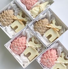 four boxes filled with assorted decorated cookies in white and pink icing on top of each other