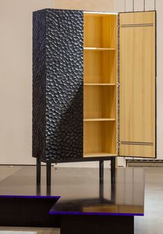 a wooden cabinet sitting on top of a black platform in front of a white wall