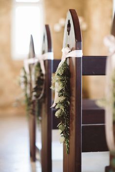 two wooden chairs decorated with greenery and bows