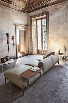 a living room filled with lots of furniture next to a large window on top of a stone floor