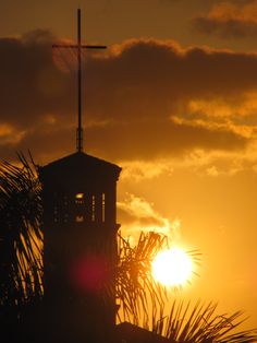 the sun is setting behind a small tower with a cross on top