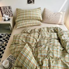 an unmade bed with plaid sheets and pillows on it, next to a black and white checkered floor